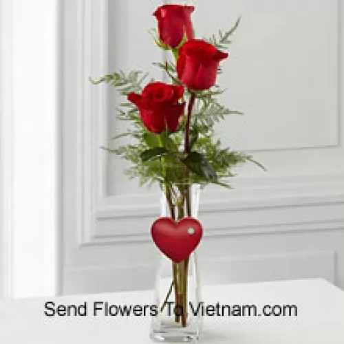 3 rote Rosen in einer Glasvase mit einem kleinen Herz daran befestigt