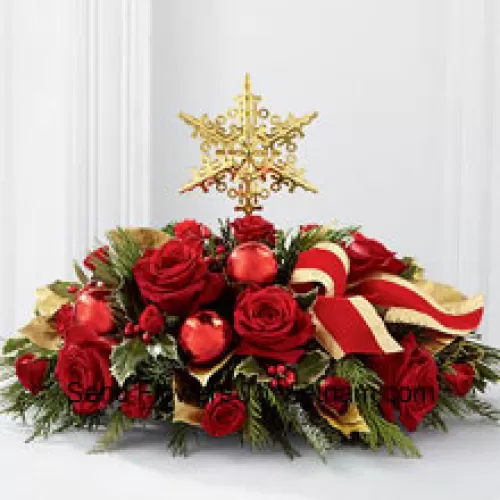 Un modo grandioso ed elegante per aggiungere bellezza alle festività. Rose rosse e spray di rose sono disposti con verdi assortiti, agrifoglio variegato, lucide palle natalizie rosse e un nastro rosso bordato d'oro, tutti circondando una cima d'albero a forma di stella dorata per creare un centro tavola natalizio unico e sofisticato. (Si prega di notare che ci riserviamo il diritto di sostituire qualsiasi prodotto con un prodotto adatto di uguale valore in caso di non disponibilità di un certo prodotto)